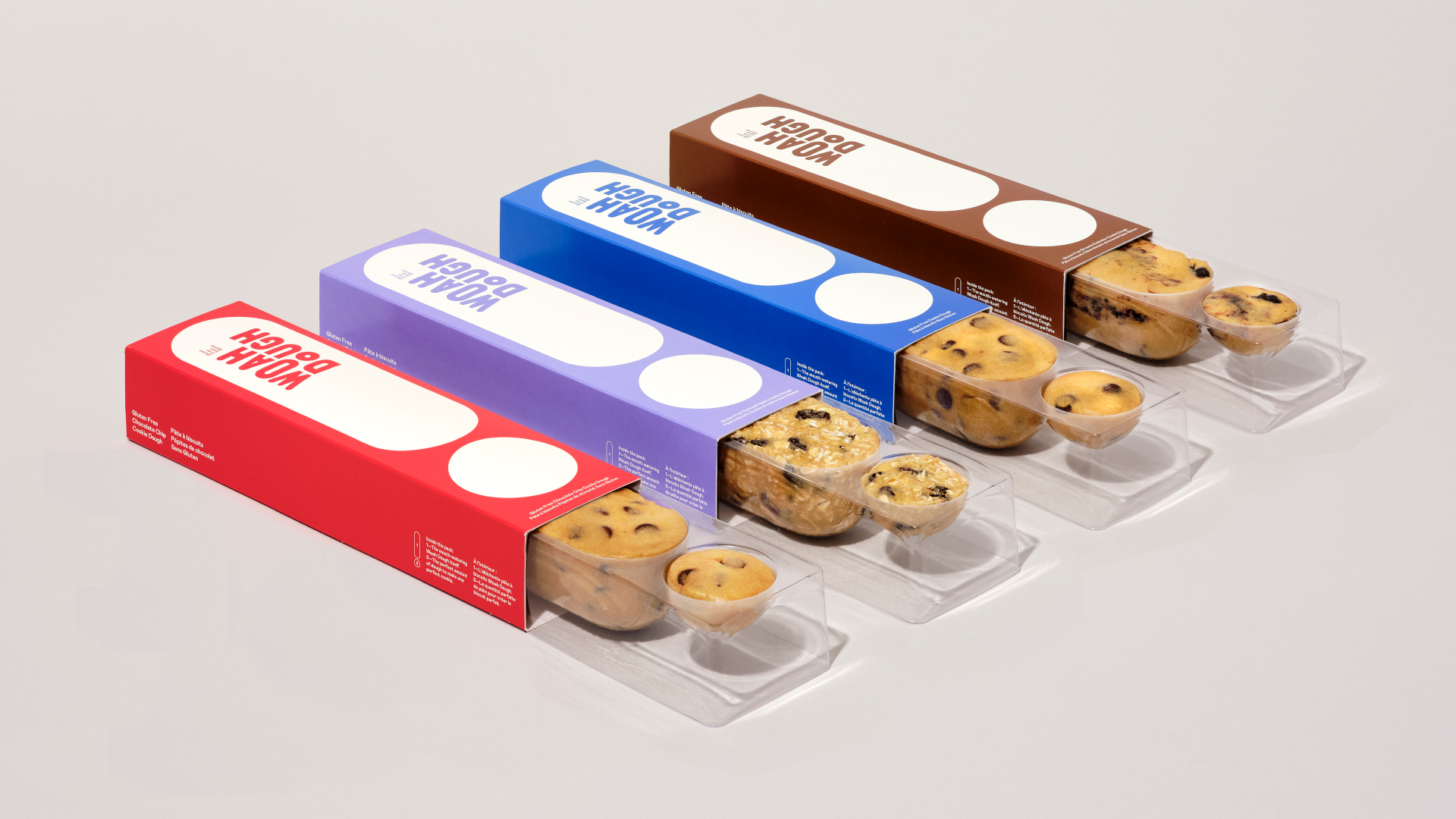 Four product packages of Woah Dough™ lined up in a row. The last one is open, and you can see the dough inside in the shape of an exclamation mark.